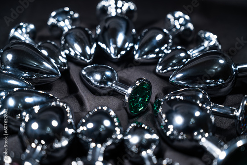 Many metal anal plugs on a black silk sheet. 