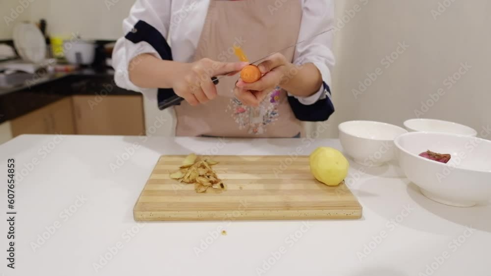 Chef grabs carrot from bowl and peels it using knife at home kitchen