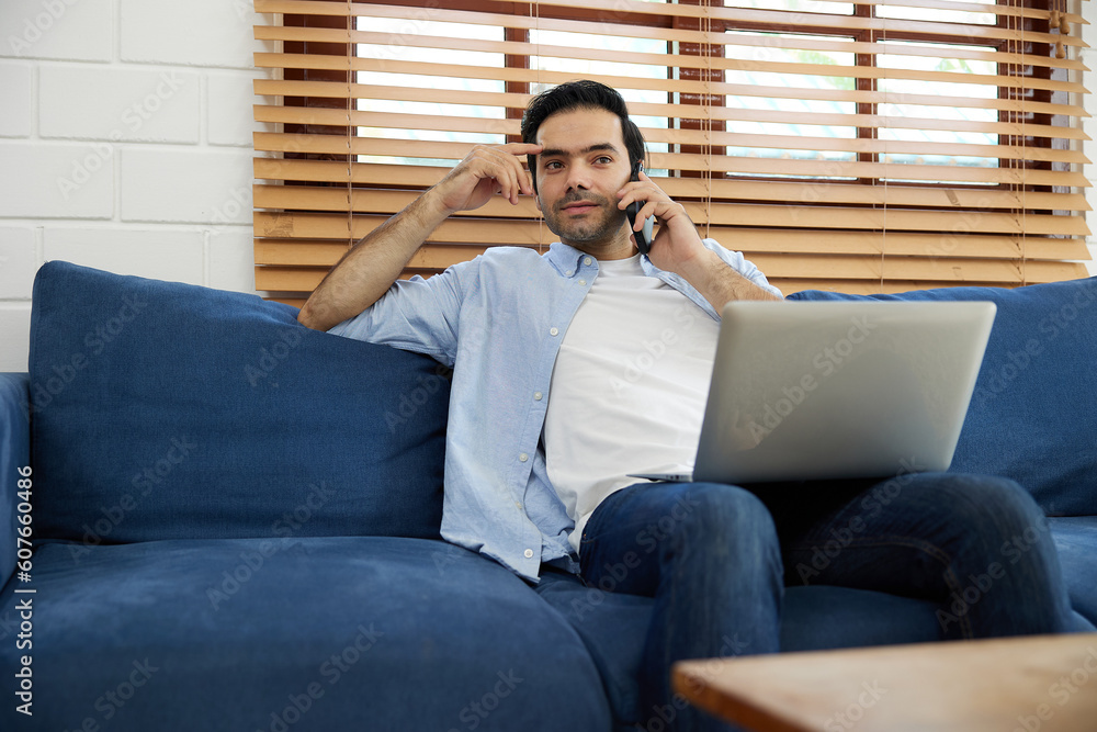 Fototapeta premium young handsome man using laptop computer and talking by smartphone at home