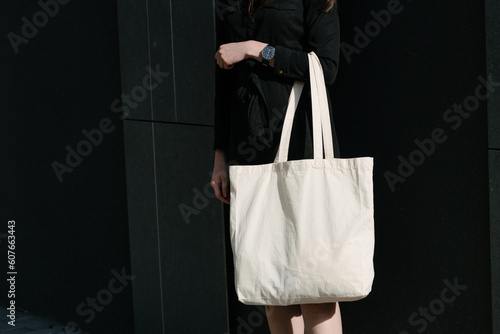 Woman holding white textile eco bag against urban city background. Ecology or environment protection concept. White eco bag for mock up.