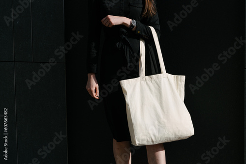 Woman holding white textile eco bag against urban city background. Ecology or environment protection concept. White eco bag for mock up.