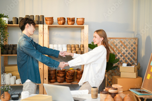 Young entrepreneur couple man and woman holding hand and swing arms while looking each other because of marketing strategy and business plan successful with handmade product on shelf background
