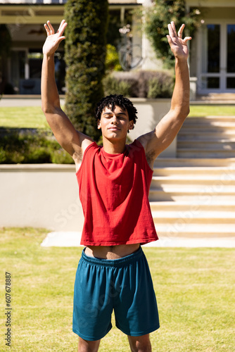 Biracial handsome young man with eyes closed and arms raised meditating in yard against house