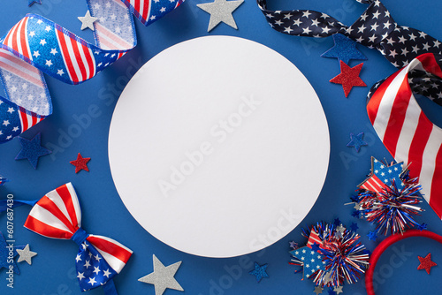 Festive decorations for celebrating Independence Day: a top view of party supplies such as ribbon, stars, headband, ties, bow-tie, placed on a blue background with a blank circle for text or ad