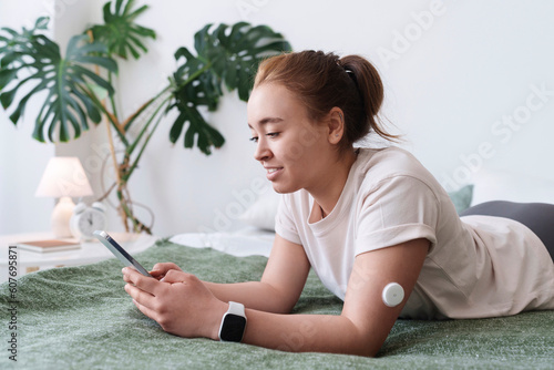 Woman with diabetes using smart phone lying on bed at home photo