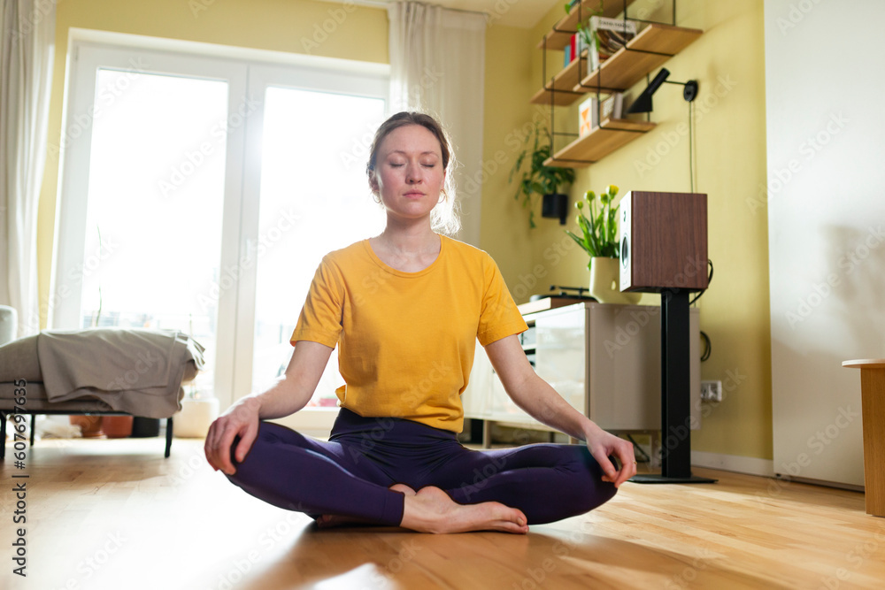 Young woman sitting cross-legged and meditating at home Young woman sitting cross-legged and meditating at home