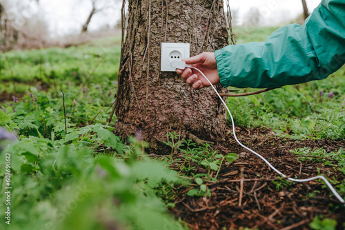 Man connecting electric plug in outlet on tree trunk