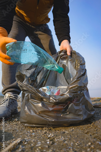 Close-up of male hand in rubber gloves picking up plastical bottle on beach. Environmental ecology pollution concept. Earth Day. photo