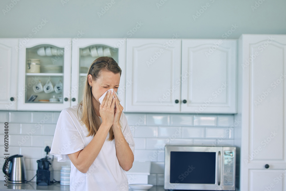 Allergies, toilet paper and woman blowing her nose in the kitchen for a cold, flu or sneeze at her home. Illness, virus and young female person with tissue for sinus, hay fever or covid in apartment.