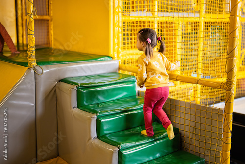 Little girl step up in stairs at yellow playground park. Child in active entertaiments. photo