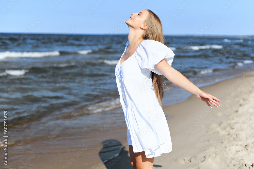 Happy smiling beautiful woman is on the ocean beach in a white summer dress, open arms. Happy smiling beautiful woman is on the ocean beach in a white summer dress, open arms.