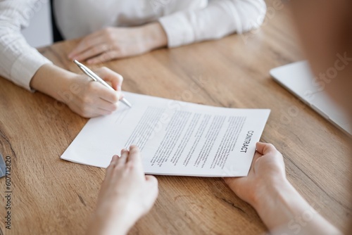 Business people signing contract papers while sitting at the wooden table in office, closeup. Partners or lawyers working together at meeting. Teamwork, partnership, success concept.