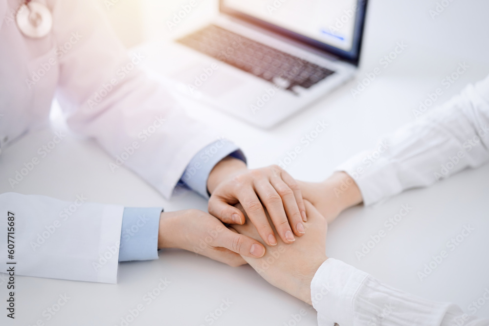 Doctor and patient sitting near each other at the table in clinic office. The focus is on female physician's hands reassuring woman, only hands, close up. Medicine concept. Doctor and patient sitting near each other at the table in clinic office. The focus is on female physician's hands reassuring woman, only hands, close up. Medicine concept.