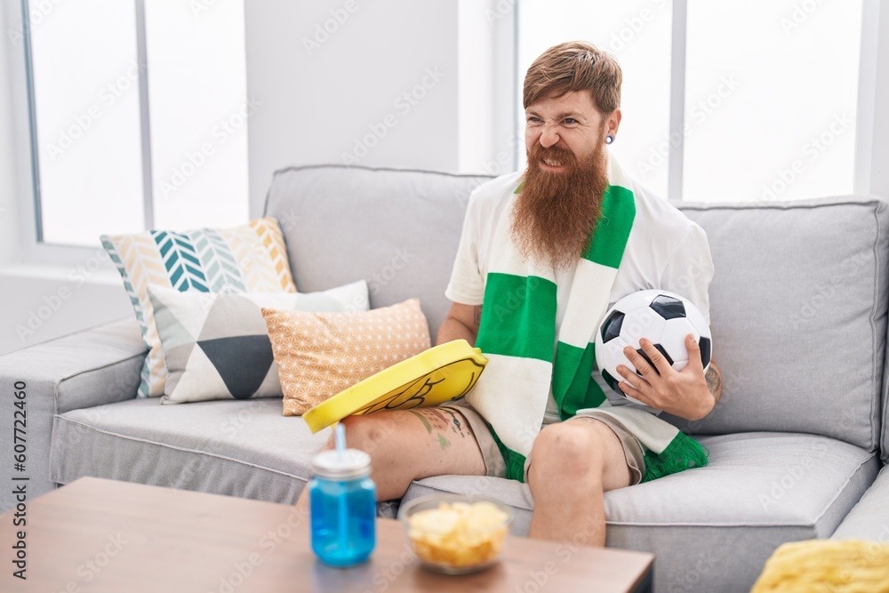 Young redhead man supporting soccer team sitting on sofa at home Young redhead man supporting soccer team sitting on sofa at home
