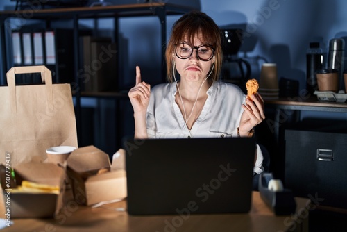 Young beautiful woman working using computer laptop and eating delivery food pointing up looking sad and upset, indicating direction with fingers, unhappy and depressed.