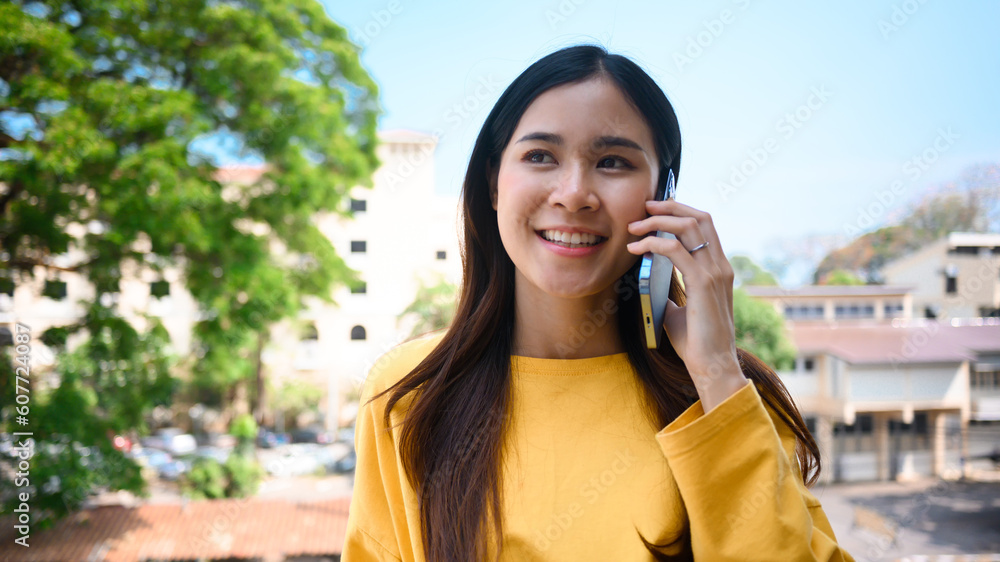 Pretty young Asian woman talking to friends on mobile phone while standing on the balcony of office building Pretty young Asian woman talking to friends on mobile phone while standing on the balcony of office building