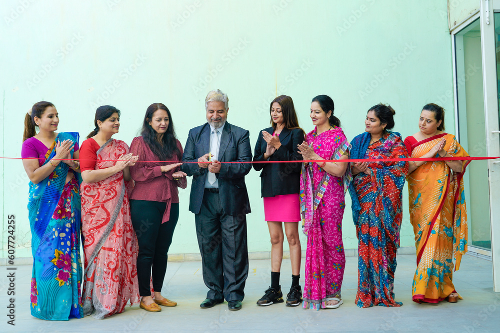 Naklejka premium Senior businessman cutting red ribbon with women employee group. inauguration concept.