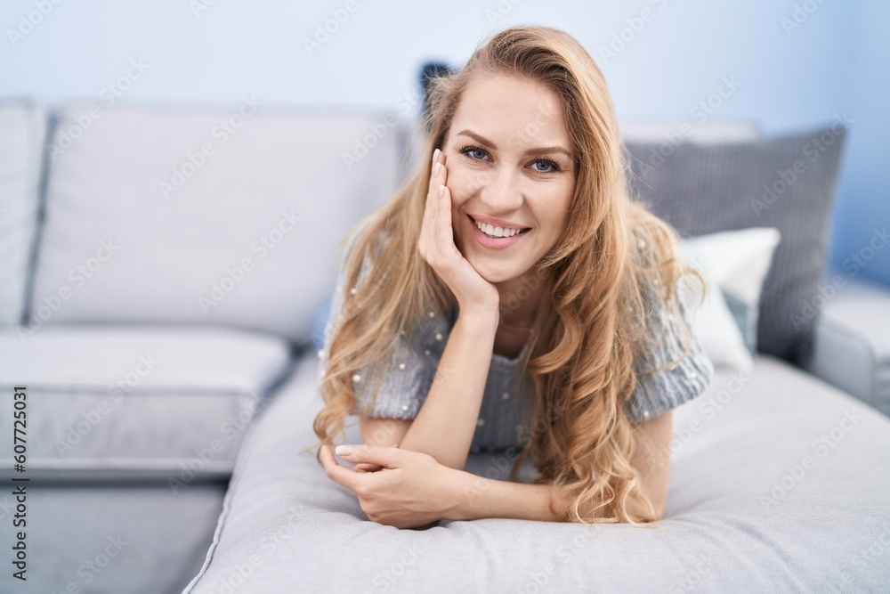 Young blonde woman smiling confident lying on sofa at home