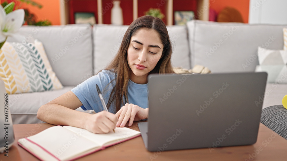 Young beautiful hispanic woman using laptop taking notes at home Young beautiful hispanic woman using laptop taking notes at home