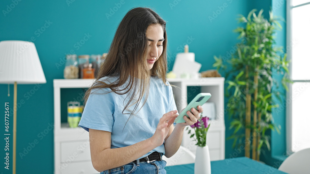 Young beautiful hispanic woman using smartphone standing at dinning room Young beautiful hispanic woman using smartphone standing at dinning room