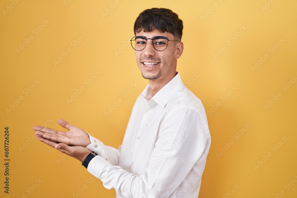 Young hispanic man standing over yellow background pointing aside with hands open palms showing copy space, presenting advertisement smiling excited happy Young hispanic man standing over yellow background pointing aside with hands open palms showing copy space, presenting advertisement smiling excited happy