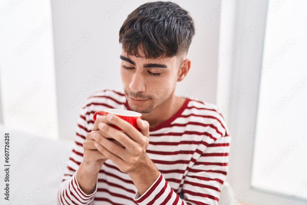 Young hispanic man smelling cup of coffee sitting on bed at bedroom Young hispanic man smelling cup of coffee sitting on bed at bedroom