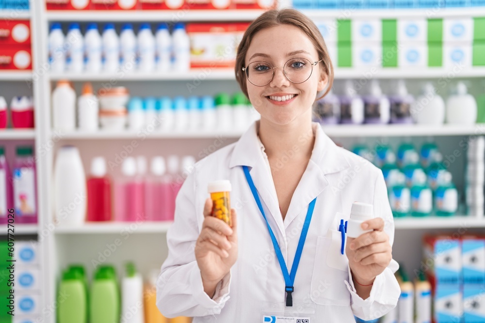 Young blonde woman pharmacist smiling confident holding two pills bottles at pharmacy Young blonde woman pharmacist smiling confident holding two pills bottles at pharmacy