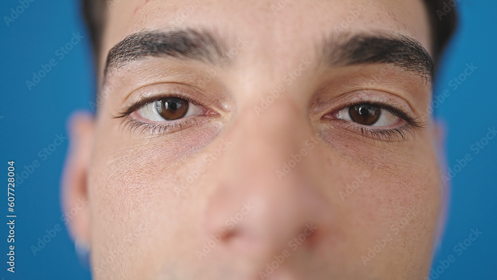 Fototapeta premium Young hispanic man standing with serious expression over isolated blue background