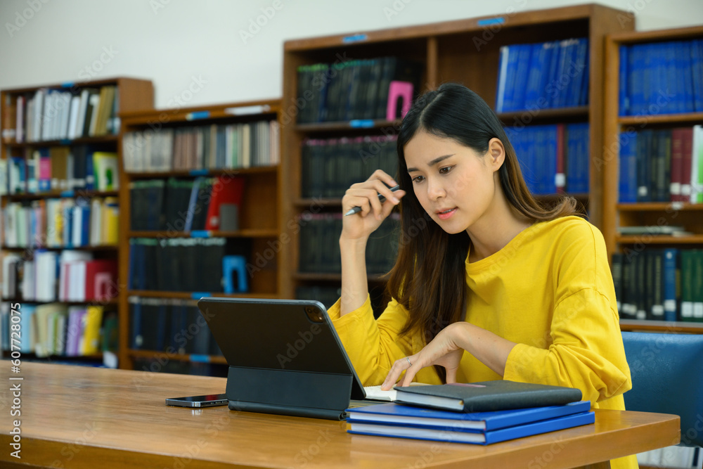 Concentrated female university student doing research on digital tablet, learning lessons, preparing for exams in library Concentrated female university student doing research on digital tablet, learning lessons, preparing for exams in library
