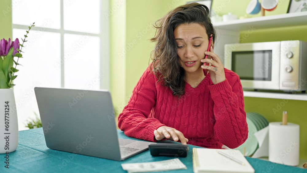 Young beautiful hispanic woman talking on smartphone accounting money at dinning room Young beautiful hispanic woman talking on smartphone accounting money at dinning room