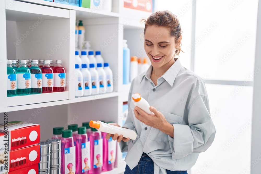 Young woman customer smiling confident holding sunscreen bottles at pharmacy