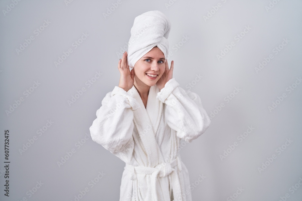 Blonde caucasian woman wearing bathrobe trying to hear both hands on ear gesture, curious for gossip. hearing problem, deaf Blonde caucasian woman wearing bathrobe trying to hear both hands on ear gesture, curious for gossip. hearing problem, deaf