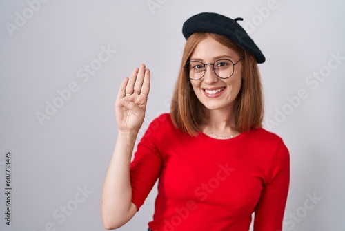 Young redhead woman standing wearing glasses and beret showing and pointing up with fingers number four while smiling confident and happy.