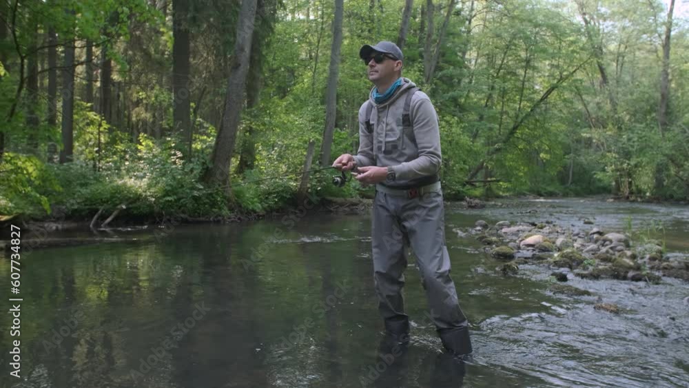 Fisherman catching brown trout on spinning tackle standing in river. Slow motion Fisherman catching brown trout on spinning tackle standing in river. Slow motion