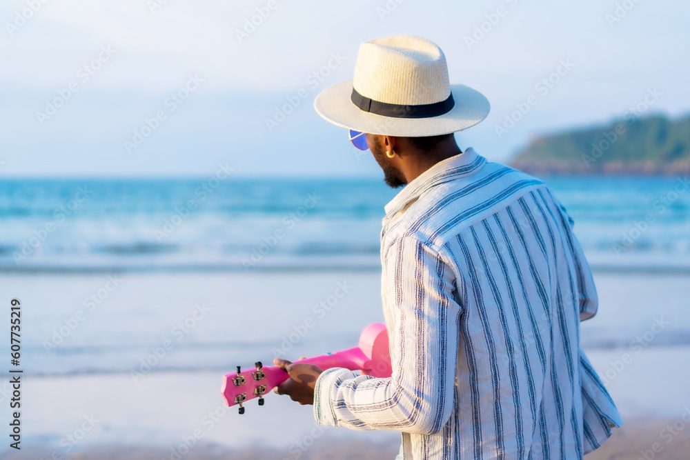 Portrait of black ethnic man enjoy summer vacation on the beach playing ukulele by the sea