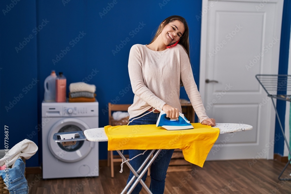Young beautiful hispanic woman talking on smartphone ironing clothes at laundry room Young beautiful hispanic woman talking on smartphone ironing clothes at laundry room