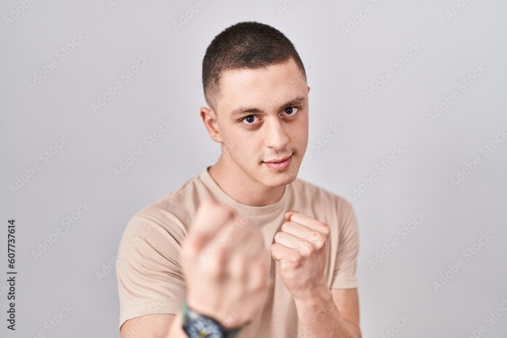 Young man standing over isolated background ready to fight with fist defense gesture, angry and upset face, afraid of problem Young man standing over isolated background ready to fight with fist defense gesture, angry and upset face, afraid of problem