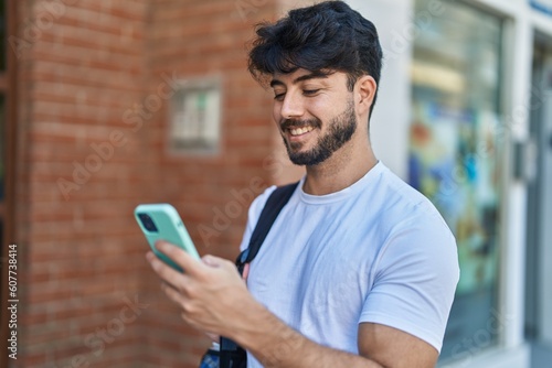 Young hispanic man wearing backpack using smartphone at street
