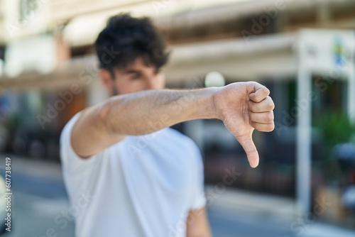 Young hispanic man doing negative sign with thumb down at street