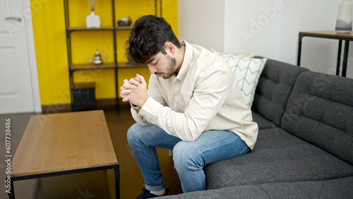 Young hispanic man stressed sitting on sofa at home