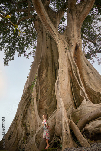 Beautiful woman next to giant ancient Cotton tree or Kapok (Ceiba pentandra) in Magra village, Bali, Indonesia.