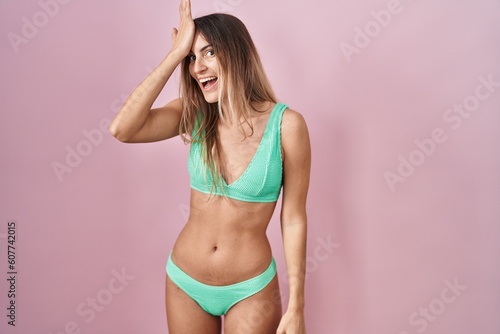 Young hispanic woman wearing bikini over pink background surprised with hand on head for mistake, remember error. forgot, bad memory concept.