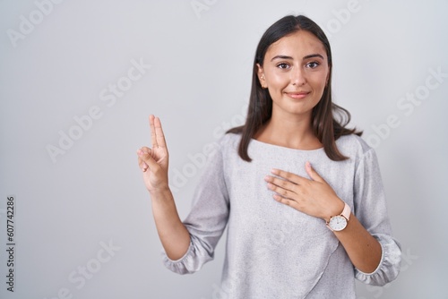 Young hispanic woman standing over white background smiling swearing with hand on chest and fingers up  making a loyalty promise oath