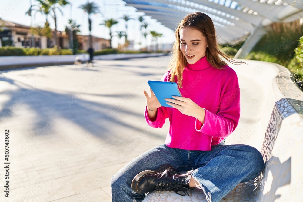 Fototapeta premium Young woman using touchpad sitting on bench at park