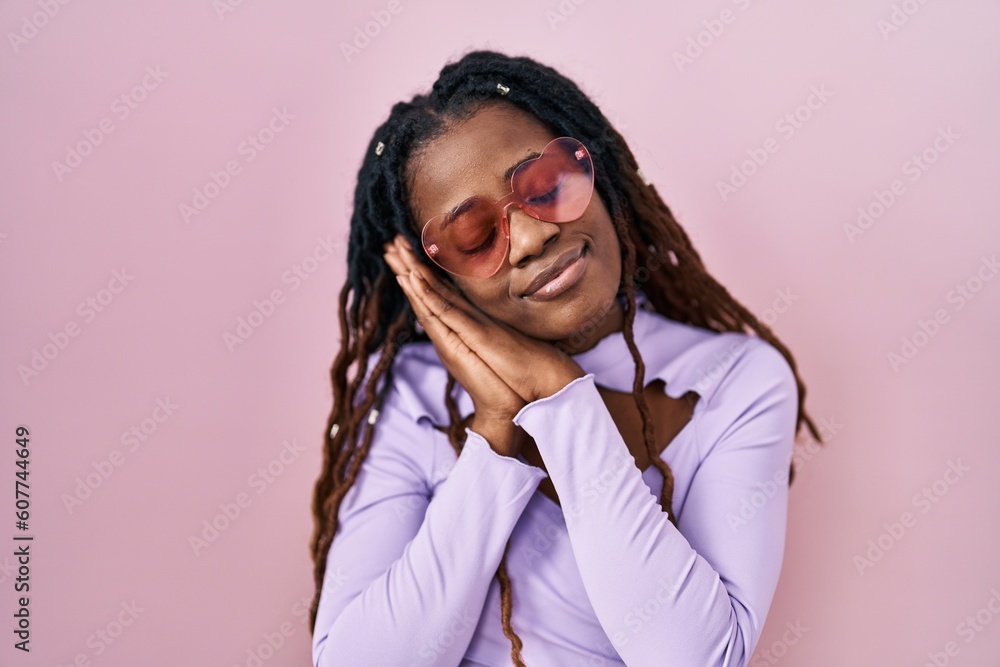 African woman with braided hair standing over pink background sleeping tired dreaming and posing with hands together while smiling with closed eyes. African woman with braided hair standing over pink background sleeping tired dreaming and posing with hands together while smiling with closed eyes.