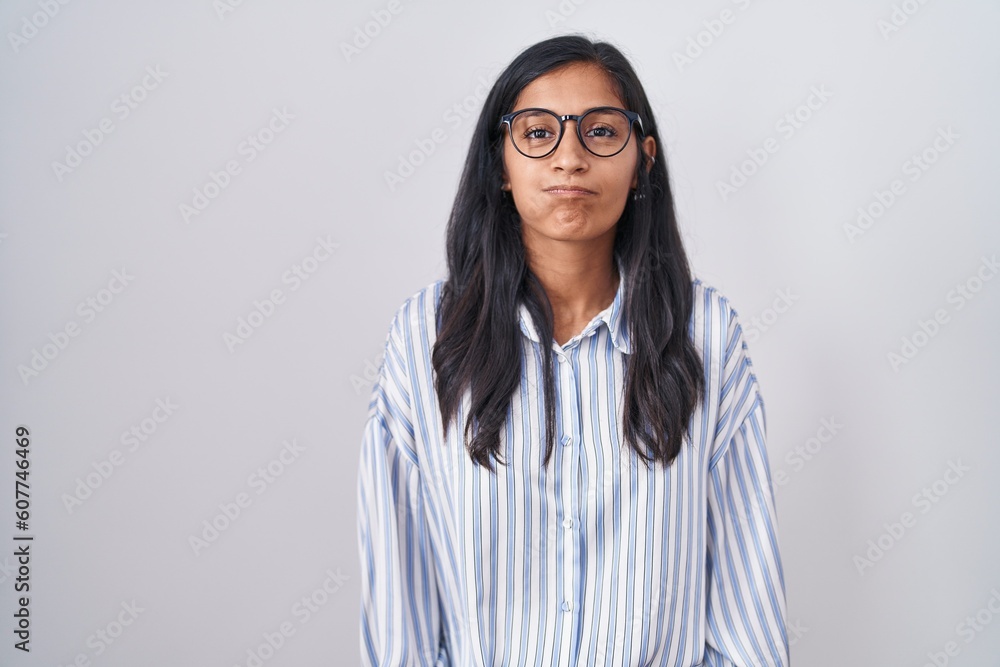 Young hispanic woman wearing glasses puffing cheeks with funny face. mouth inflated with air, crazy expression. Young hispanic woman wearing glasses puffing cheeks with funny face. mouth inflated with air, crazy expression.