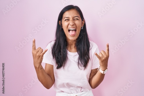 Young hispanic woman standing over pink background shouting with crazy expression doing rock symbol with hands up. music star. heavy music concept.