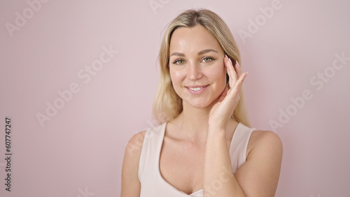 Young blonde woman smiling confident touching face over isolated pink background