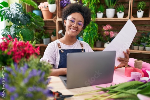 African american woman florist using laptop reading document at flower shop