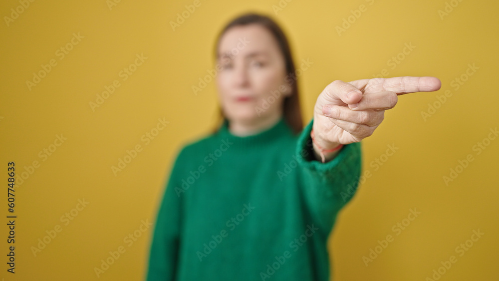 Mature hispanic woman with grey hair pointing to blank space with angry face over isolated yellow background Mature hispanic woman with grey hair pointing to blank space with angry face over isolated yellow background